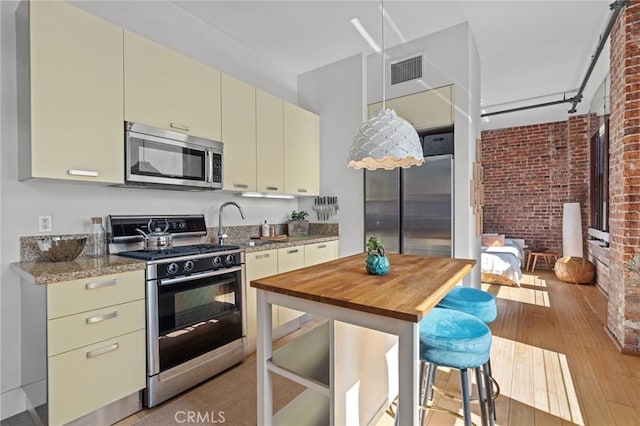 460 S Spring St Unit 302, Los Angeles, CA 90013 - kitchen with a sink, stainless steel appliances, cream cabinets, visible vents, and brick wall