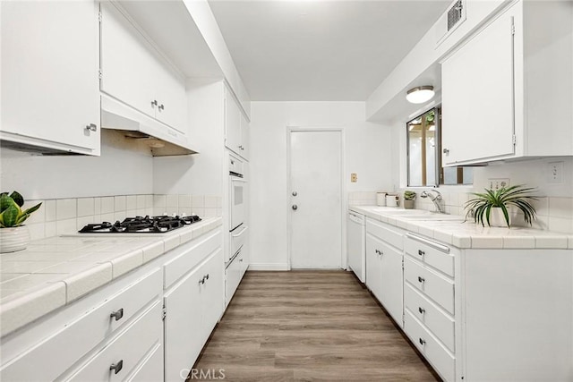 28 Brisbane Way, Irvine, CA 92612 - kitchen with white appliances, tile countertops, white cabinetry, light wood-style floors, and backsplash