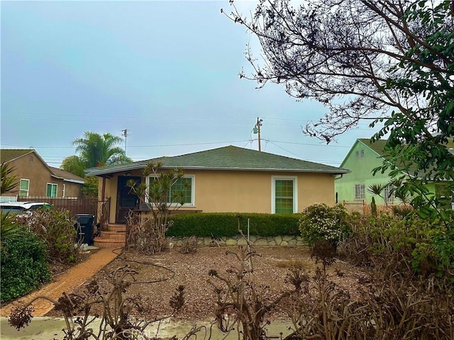single story home featuring fence, stucco siding, and roof with shingles