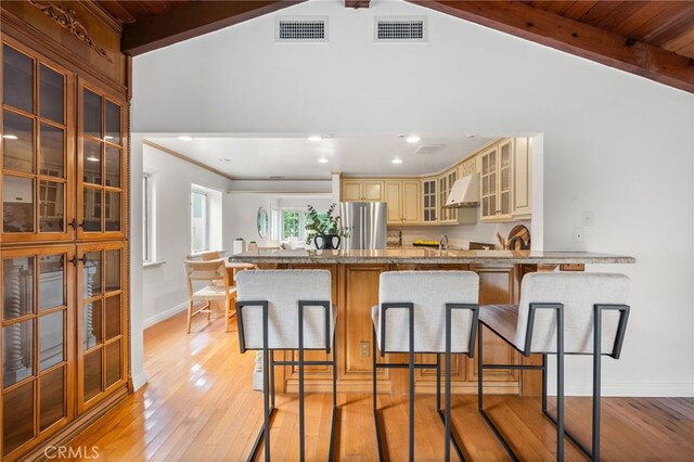 3569 Kelton Ave, Los Angeles, CA 90034 - kitchen with freestanding refrigerator, cream cabinetry, under cabinet range hood, light wood-style floors, and a kitchen bar