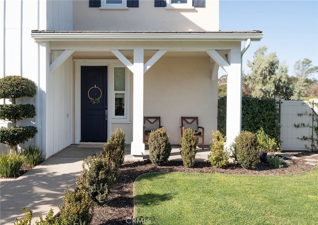 entrance to property featuring a lawn, fence, board and batten siding, and stucco siding