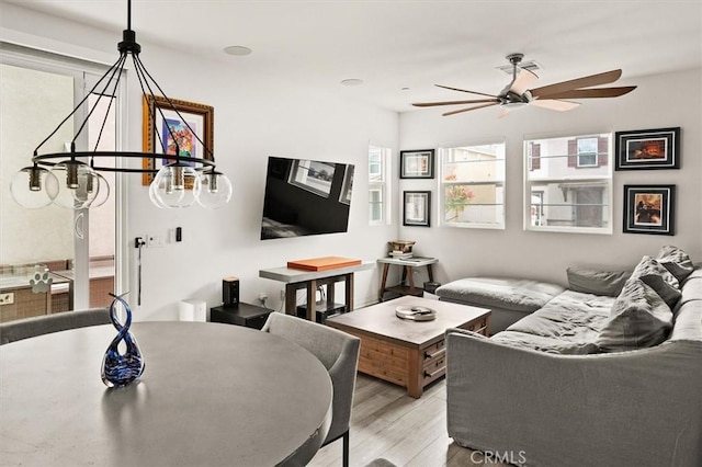 living area featuring ceiling fan with notable chandelier and light wood-type flooring