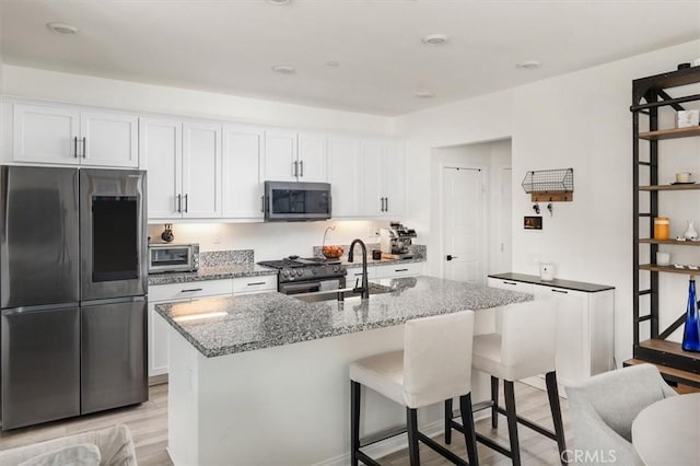 kitchen with a sink, light stone counters, appliances with stainless steel finishes, and white cabinets