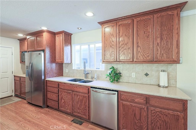 kitchen featuring decorative backsplash, brown cabinets, stainless steel appliances, a sink, and light wood-style floors