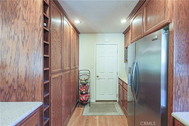 kitchen with a textured ceiling, light stone countertops, open shelves, light wood-style floors, and stainless steel fridge with ice dispenser
