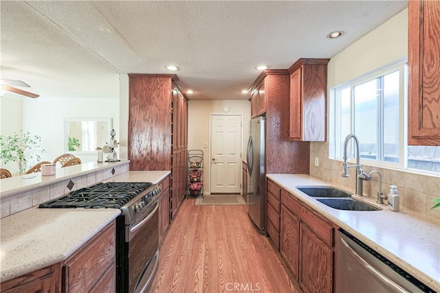 kitchen featuring light wood finished floors, tasteful backsplash, appliances with stainless steel finishes, a sink, and brown cabinetry