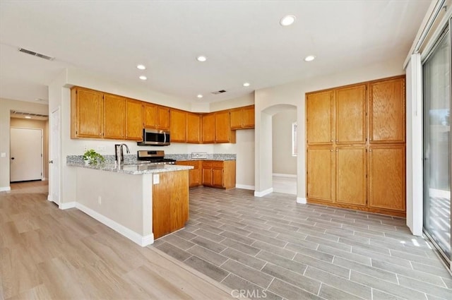 23403 Mountain Song, Murrieta, CA 92562 - kitchen featuring baseboards, a peninsula, brown cabinetry, stainless steel appliances, and arched walkways