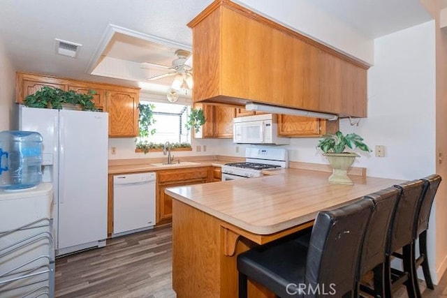 kitchen featuring light countertops, a peninsula, white appliances, ceiling fan, and a sink