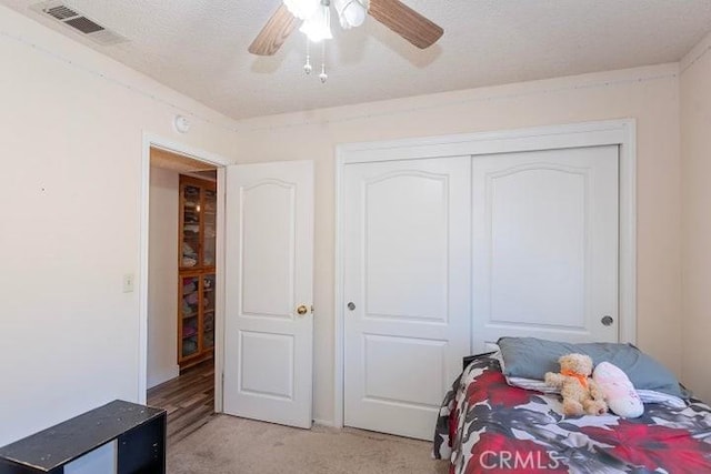 bedroom with a textured ceiling, ceiling fan, visible vents, light carpet, and a closet