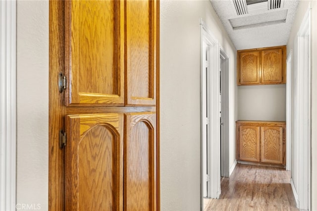 hall with visible vents, light wood-style flooring, and a textured ceiling