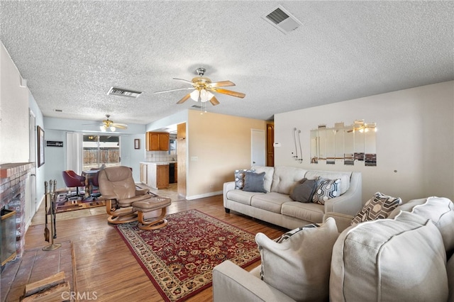 living room with visible vents, light wood-style floors, a fireplace, and a ceiling fan