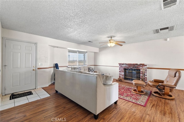 living area with a fireplace, ceiling fan, visible vents, and wood finished floors