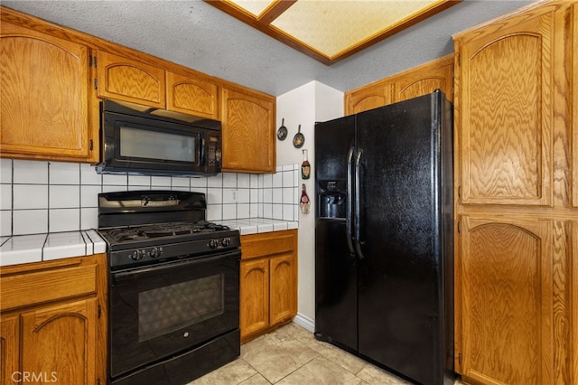 kitchen featuring brown cabinetry, black appliances, and tile counters