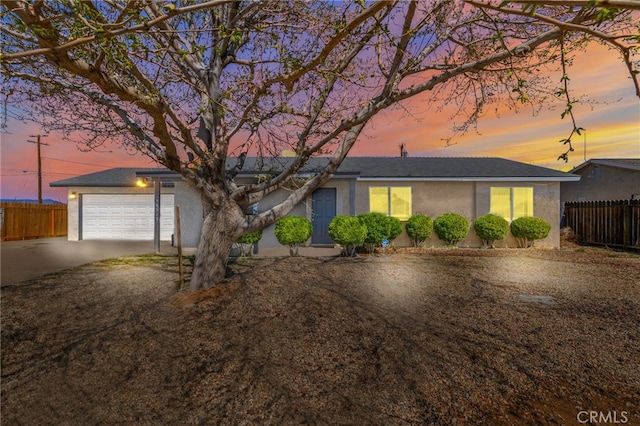 ranch-style home with concrete driveway, stucco siding, fence, and an attached garage