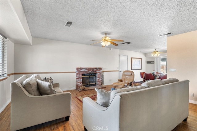 living room featuring a brick fireplace, visible vents, wood finished floors, and a ceiling fan