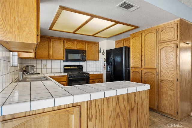 kitchen featuring a sink, tile countertops, black appliances, and visible vents