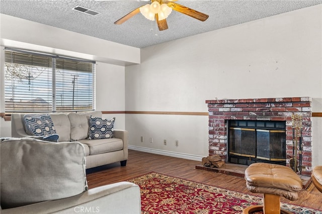 living room featuring a textured ceiling, visible vents, baseboards, wood finished floors, and a ceiling fan
