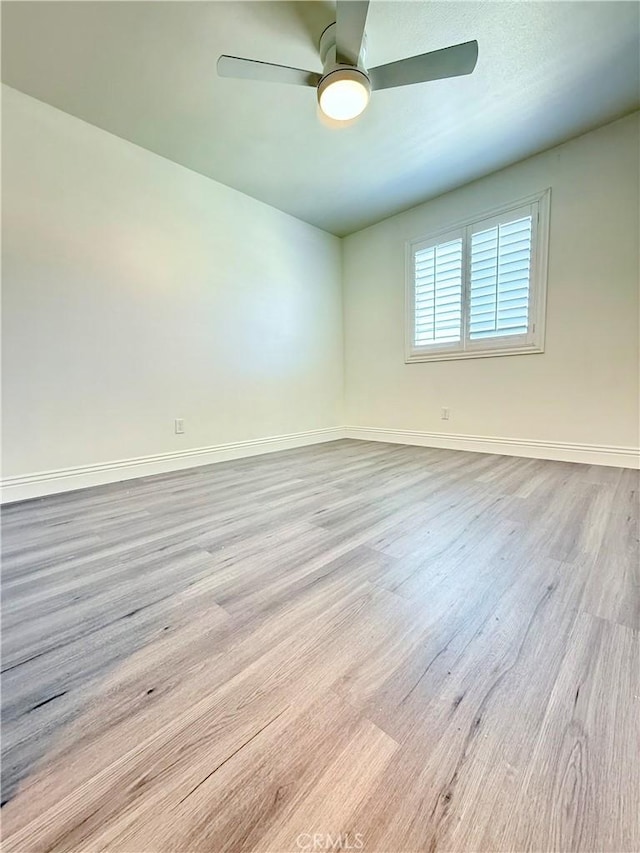 spare room with baseboards, wood finished floors, and a ceiling fan