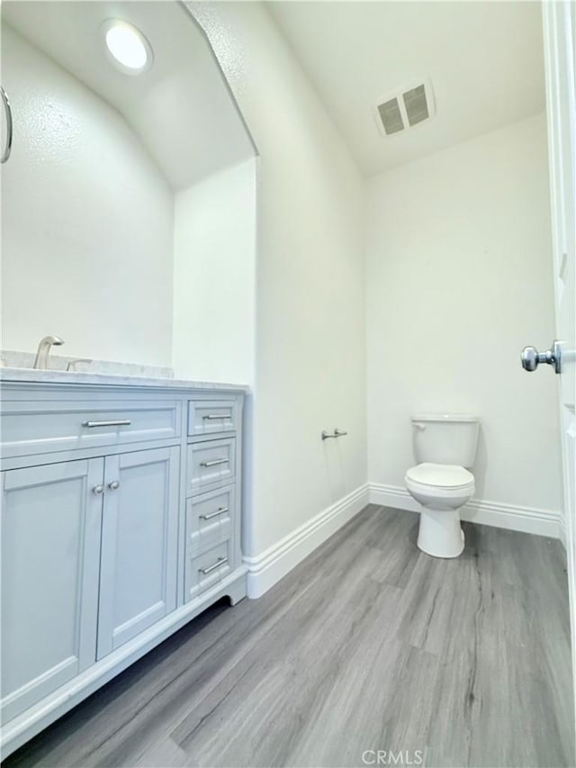 bathroom with wood finished floors, toilet, vanity, baseboards, and visible vents