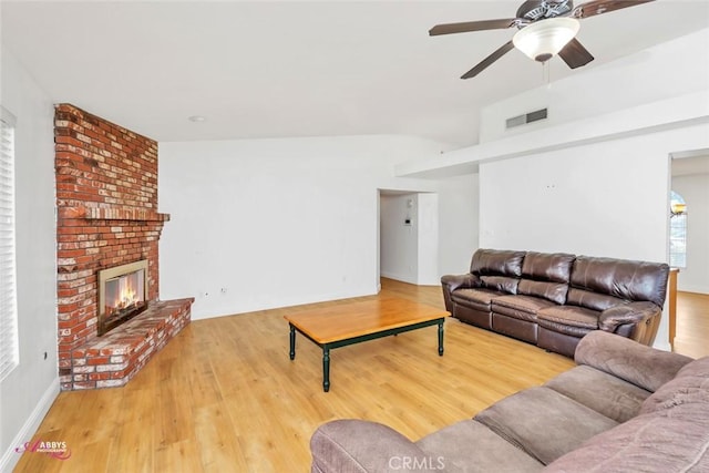 living area with a brick fireplace, vaulted ceiling, visible vents, a ceiling fan, and wood finished floors