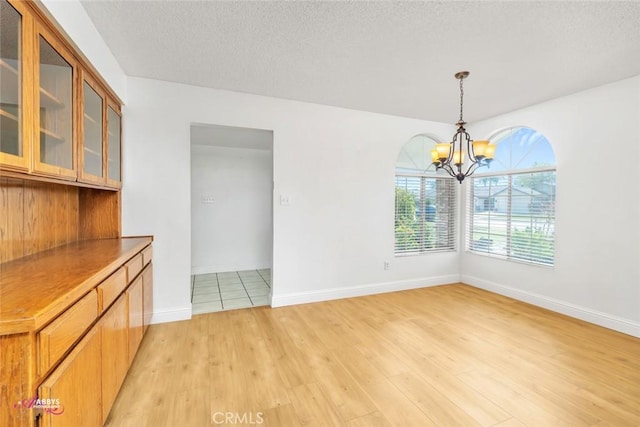 unfurnished dining area featuring light wood finished floors, a textured ceiling, baseboards, and a chandelier