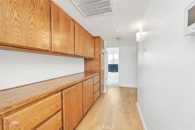 corridor with light wood-style flooring, a textured ceiling, baseboards, and visible vents