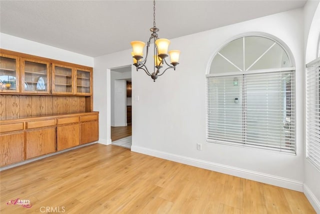 unfurnished dining area featuring light wood finished floors, baseboards, and a chandelier