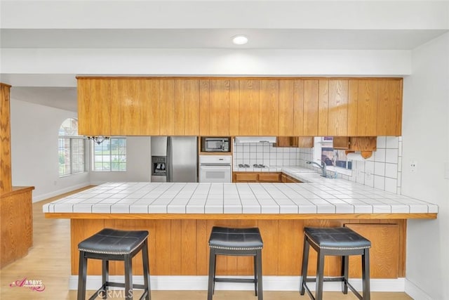 kitchen with a peninsula, brown cabinets, appliances with stainless steel finishes, a sink, and backsplash