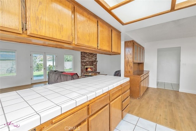 kitchen with light tile patterned flooring, a fireplace, brown cabinetry, baseboards, and tile countertops