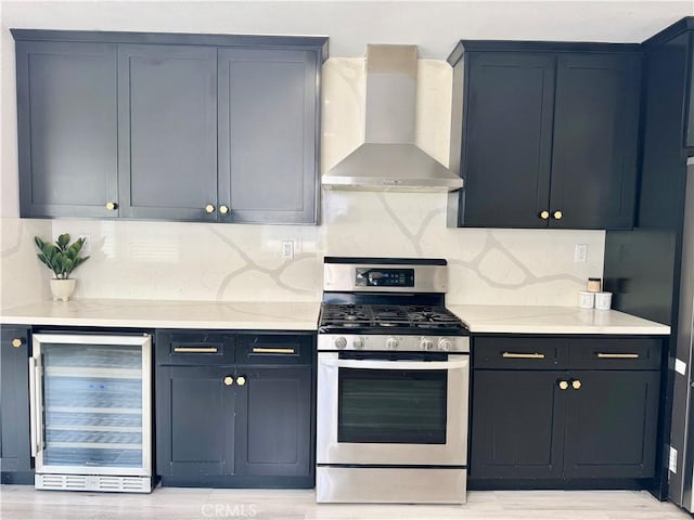 kitchen featuring wall chimney range hood, light countertops, wine cooler, and stainless steel gas range oven