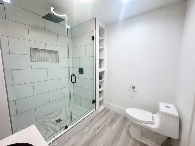 bathroom featuring baseboards, wood finished floors, toilet, and a shower stall