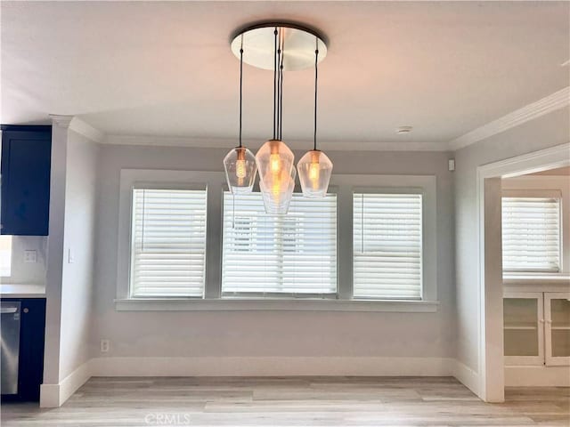 unfurnished dining area featuring baseboards, light wood-style flooring, ornamental molding, and an inviting chandelier