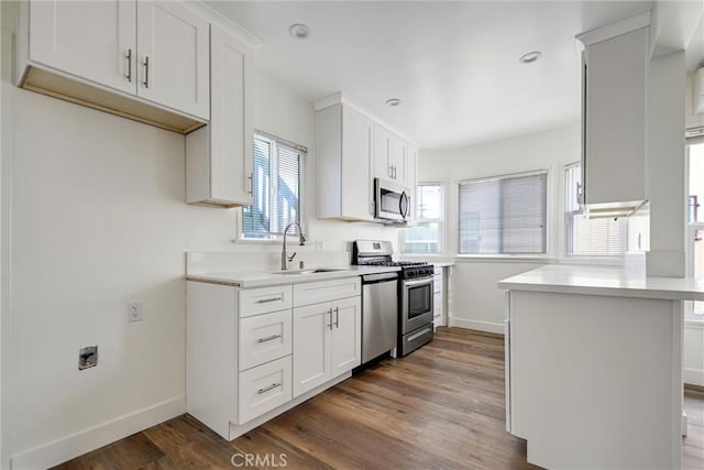 kitchen with dark wood-style flooring, light countertops, white cabinets, appliances with stainless steel finishes, and a sink