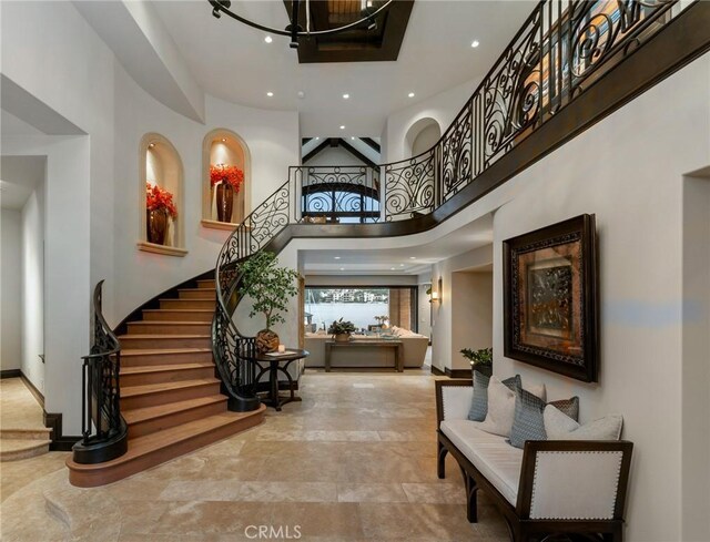 foyer entrance with a towering ceiling, recessed lighting, a chandelier, stairs, and baseboards