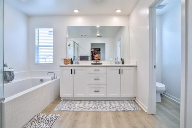 bathroom featuring double vanity, a garden tub, a stall shower, toilet, and wood finished floors
