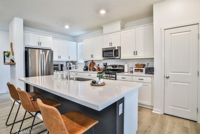 kitchen with tasteful backsplash, a sink, stainless steel appliances, a kitchen bar, and light wood finished floors