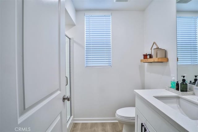 bathroom with vanity, toilet, a shower with shower door, baseboards, and wood finished floors