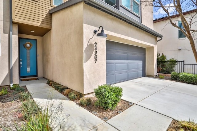 view of exterior entry with concrete driveway, a garage, stucco siding, and fence