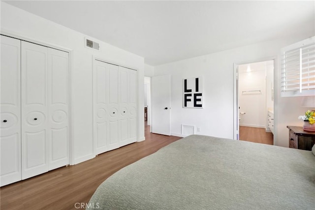 bedroom with two closets, ensuite bath, wood finished floors, and visible vents