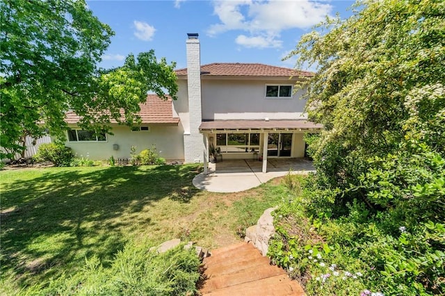 rear view of property with a tiled roof, a chimney, a lawn, a patio, and stucco siding
