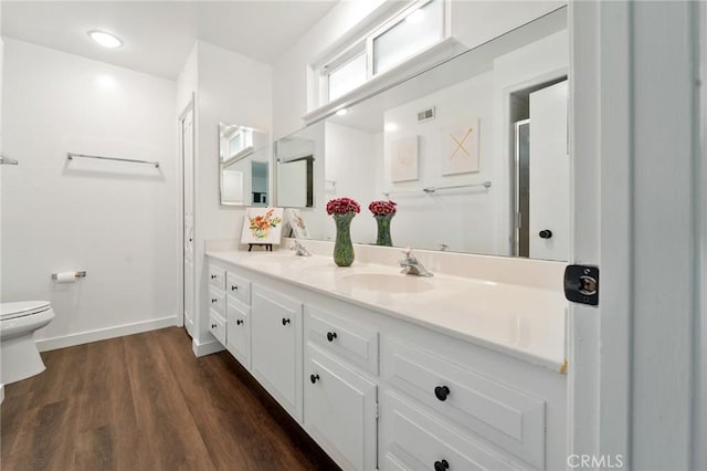 full bath with double vanity, wood finished floors, a sink, baseboards, and toilet