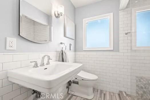 bathroom with tile walls, wainscoting, toilet, a sink, and wood finished floors