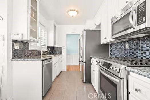 kitchen with white cabinetry, a sink, appliances with stainless steel finishes, and glass insert cabinets