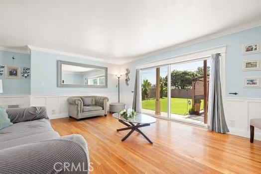 living room featuring a wainscoted wall, crown molding, wood finished floors, and a decorative wall