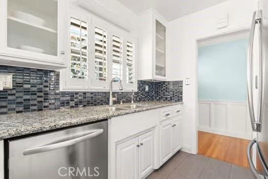 kitchen featuring a sink, white cabinetry, light stone countertops, wood finished floors, and appliances with stainless steel finishes