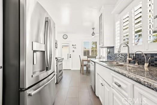 kitchen featuring white cabinetry, stainless steel appliances, decorative backsplash, a sink, and stone countertops