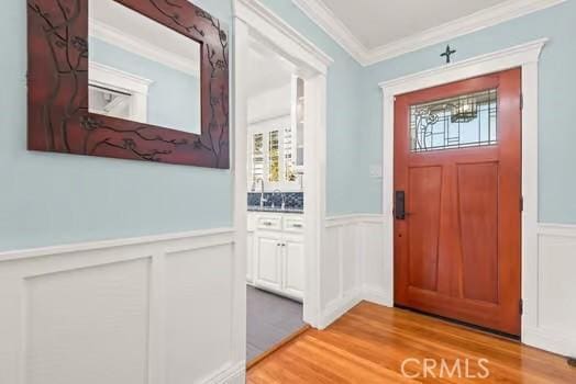 foyer with light wood-type flooring, a wainscoted wall, ornamental molding, and a wealth of natural light