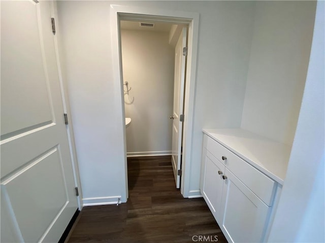 hall with baseboards, visible vents, and dark wood-type flooring
