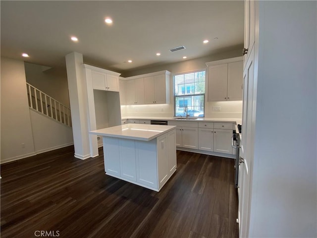 kitchen with light countertops, a kitchen island, visible vents, white cabinets, and dark wood-style flooring