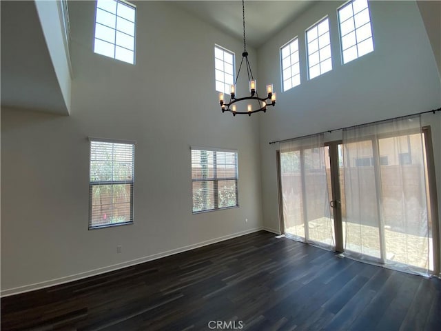 empty room with a notable chandelier, dark wood-style floors, and baseboards
